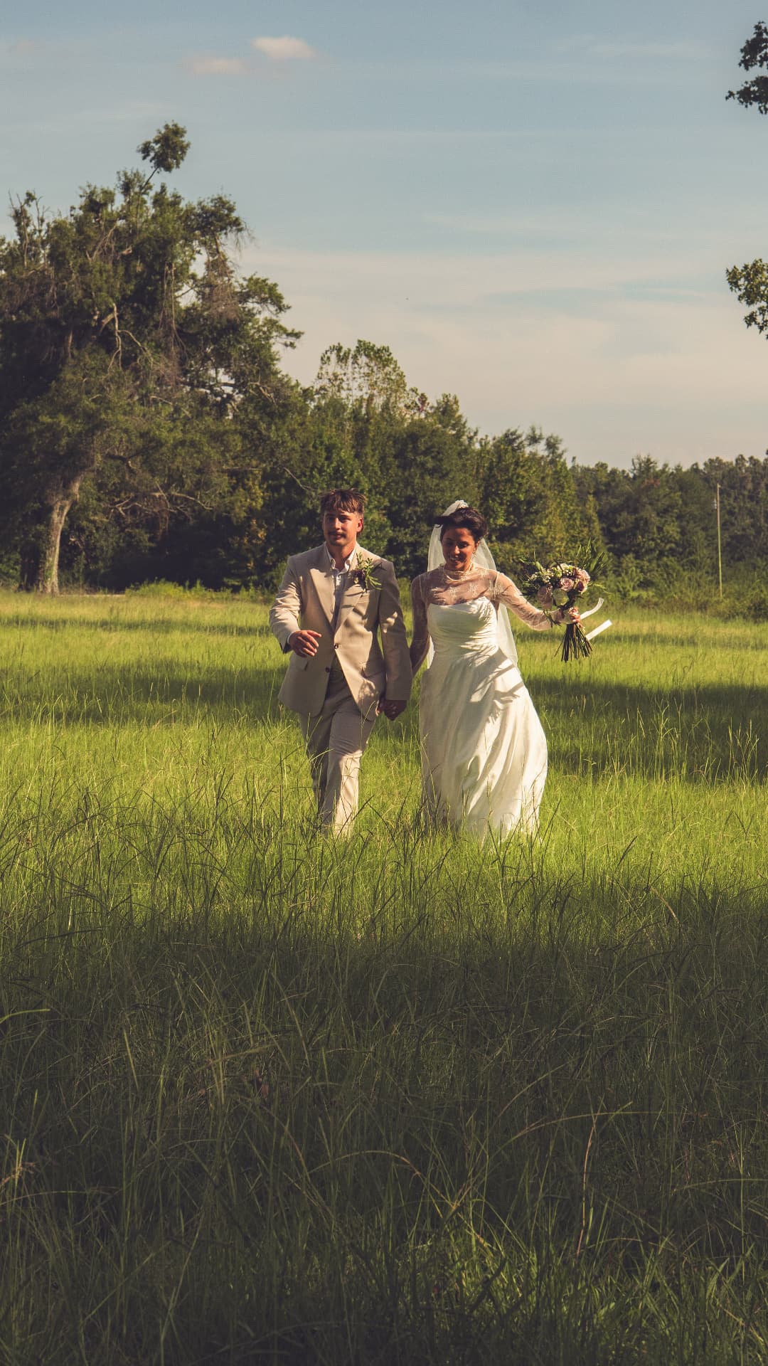 A bride and groom walking hand in hand through a green field